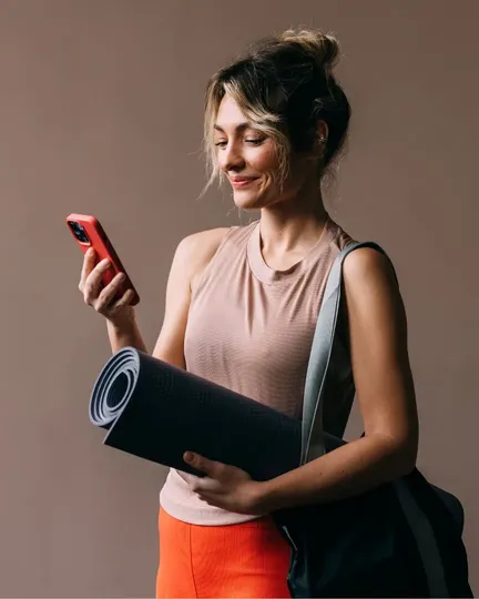 Alumna sonriendo con el móvil y una esterilla de yoga